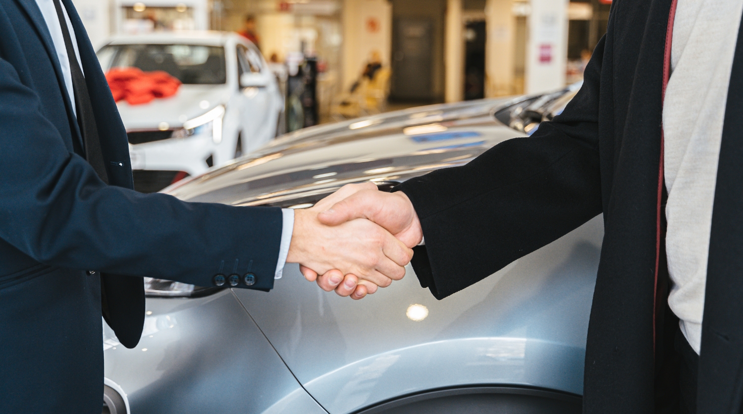 A dealership representative shaking hands with a customer in a showroom to symbolize a successful DMS-driven sales appointment.